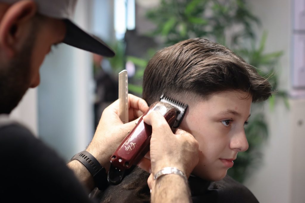 A teenager boy is trimmed in the barbershop. A barber is cutting the teenager boy.