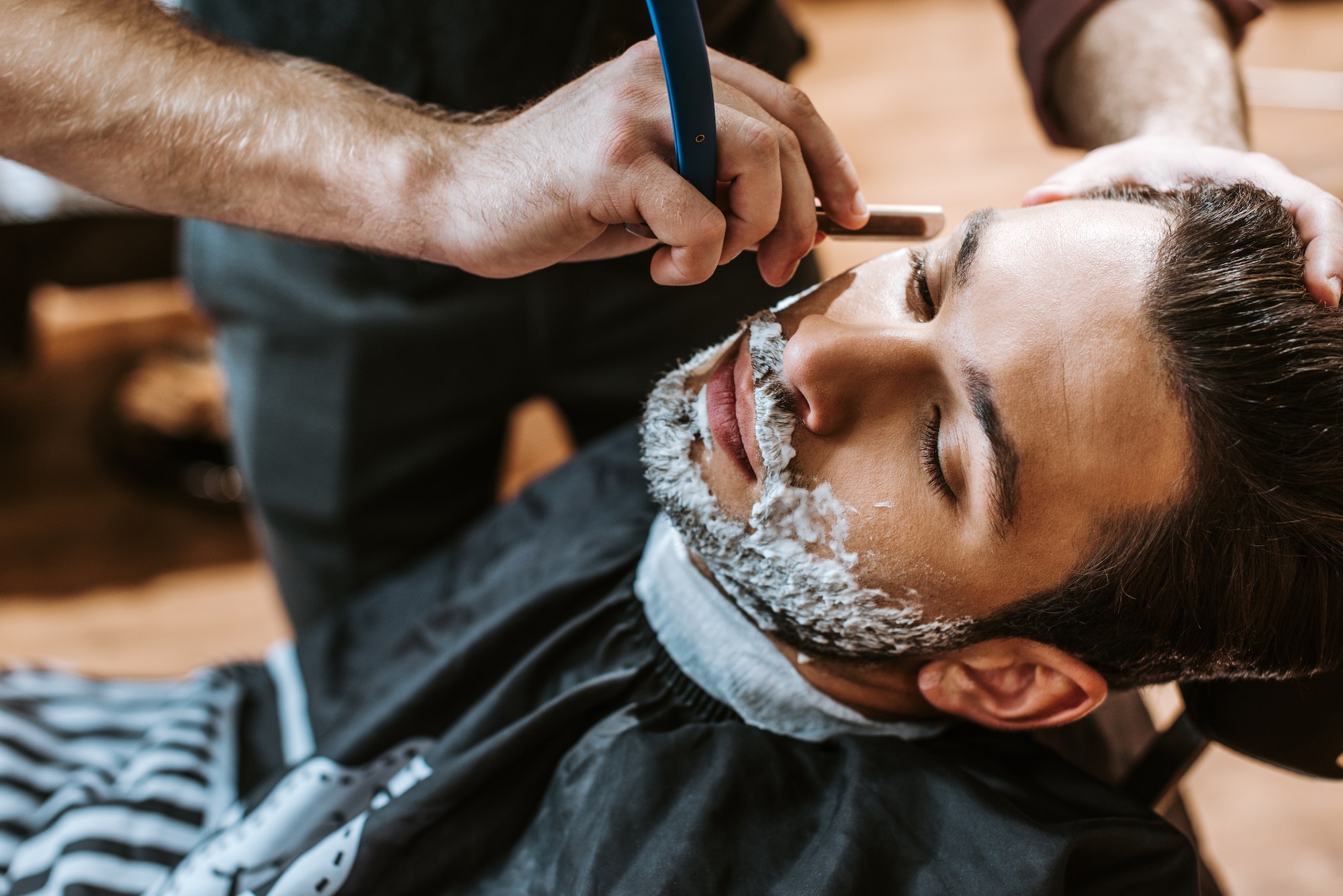 barber shaving bearded man with shaving cream on face