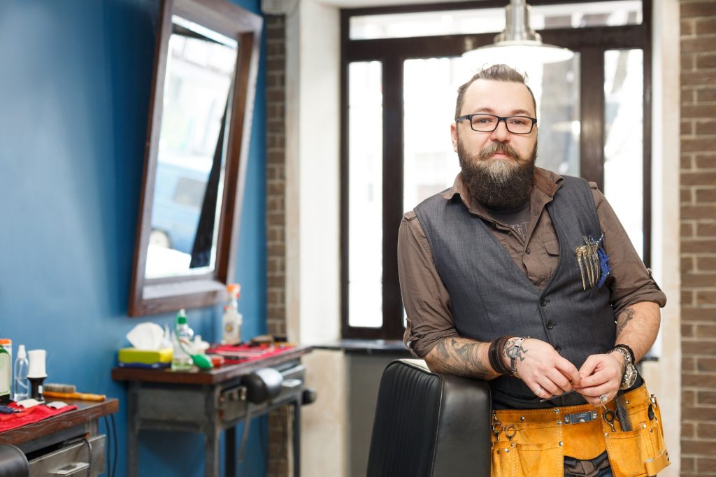 Bearded barber posing to camera at barbershop