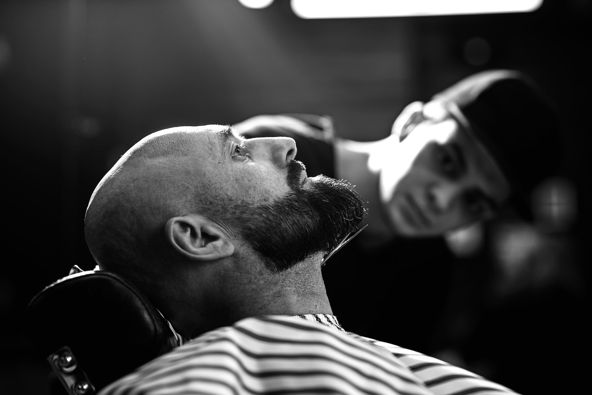 Black and white photo. Fashion barber dressed in a black clothes tidies up men's beard and